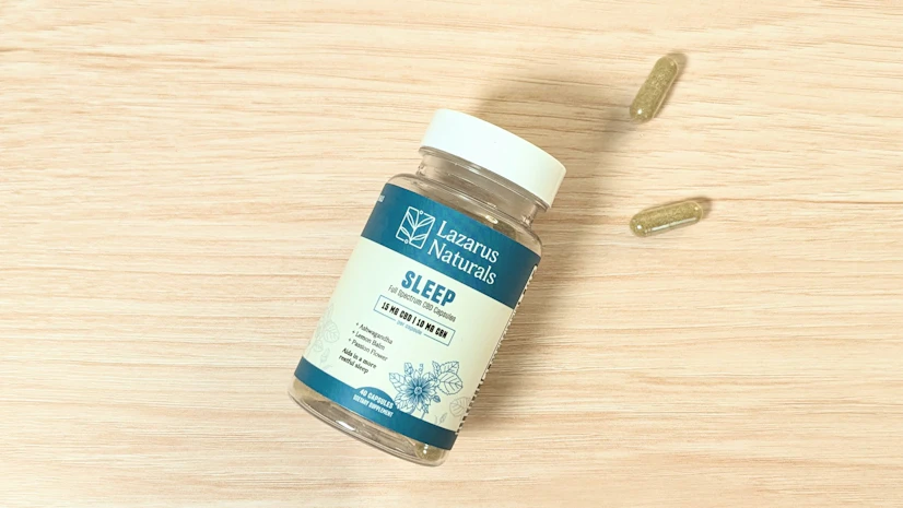 A bottle of Lazarus Naturals Sleep Full-Spectrum CBD + CBN Capsules on a wood surface.