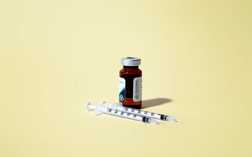 Vial of AOD-9604 peptide with two syringes against a yellow background.