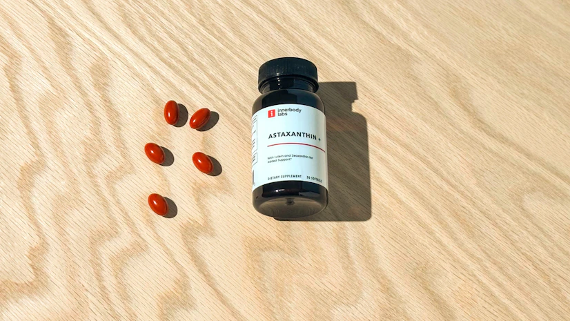 Overhead view of a Innerbody Labs Astaxanthin+ bottle on a tabletop with capsules beside it