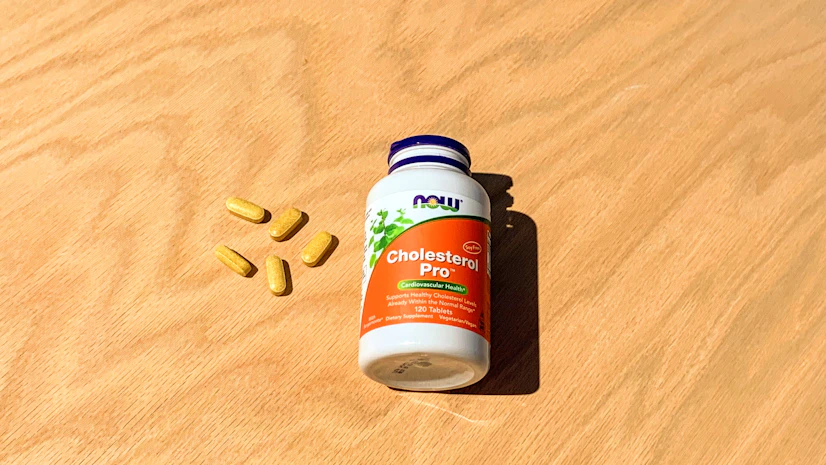 Overhead view of a NOW Cholesterol Pro bottle on a tabletop with tablets beside it