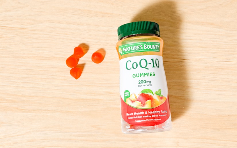 A bottle of Nature’s Bounty CoQ10 Gummies sits on a wood surface with several gummies next to it