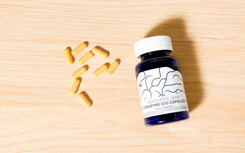 A bottle of Nootropics Depot CoQ10 capsules sits on a wood surface with several capsules next to it