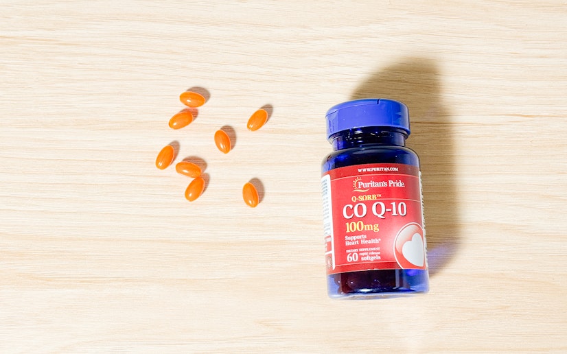 A bottle of Puritan's Pride QSorb CoQ10 sits on a wood surface with several softgels next to it