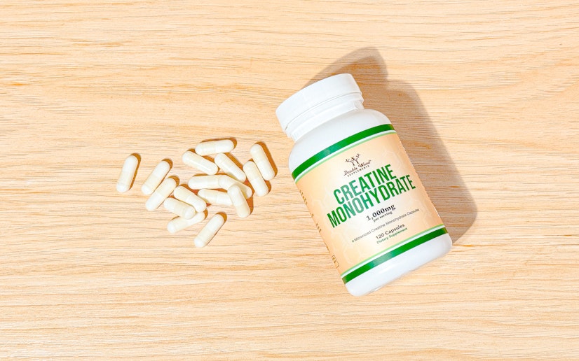 Bottle of Double Wood Creatine Monohydrate lays on a wood surface with several capsules poured out