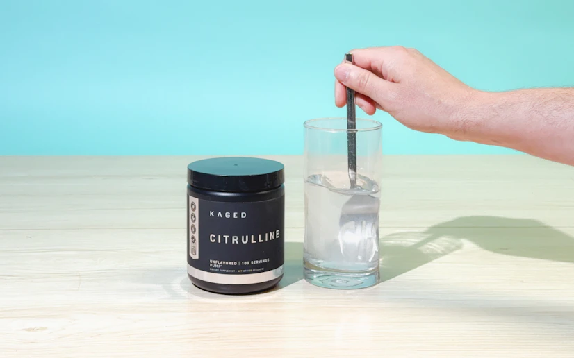 Kaged L-citrulline being stirred into water in a glass next to the tub it comes in.