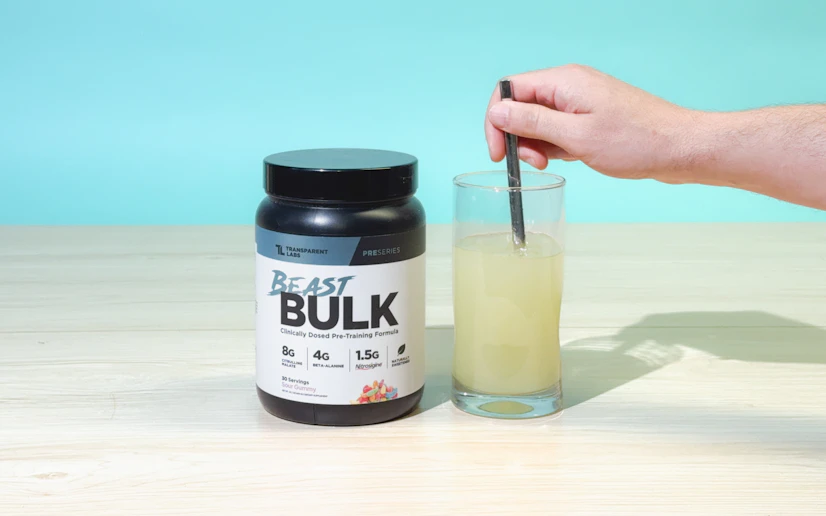 Transparent Labs Beast Bulk tub with a glass into which a hand is stirring the powdered supplement