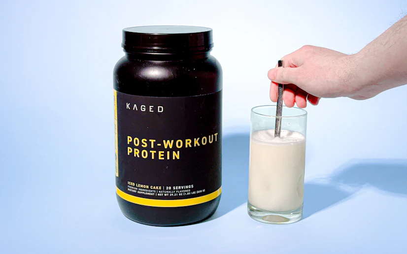 Kaged Post-Workout Protein mixed in a glass next to its container against a blue background