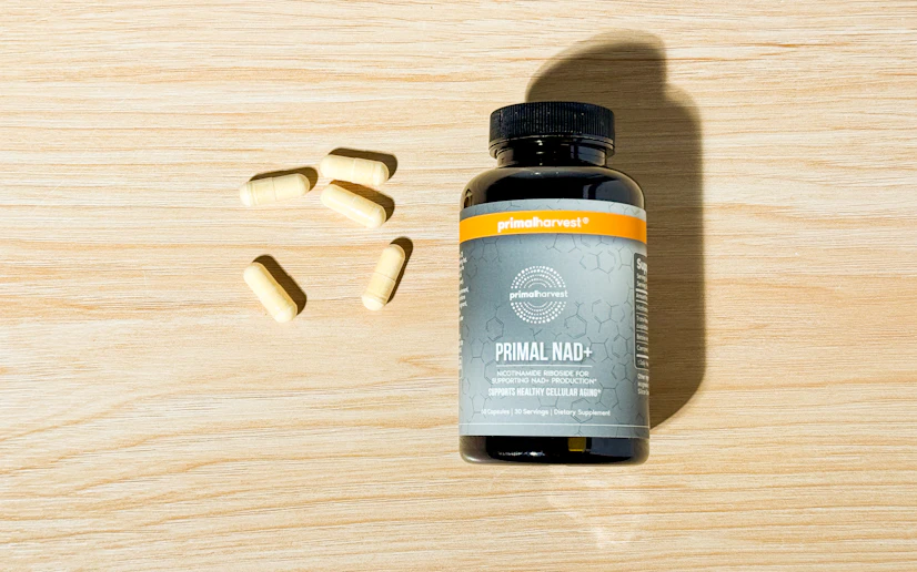 Primal Harvest Primal NAD+ bottle and capsules on a wood surface.