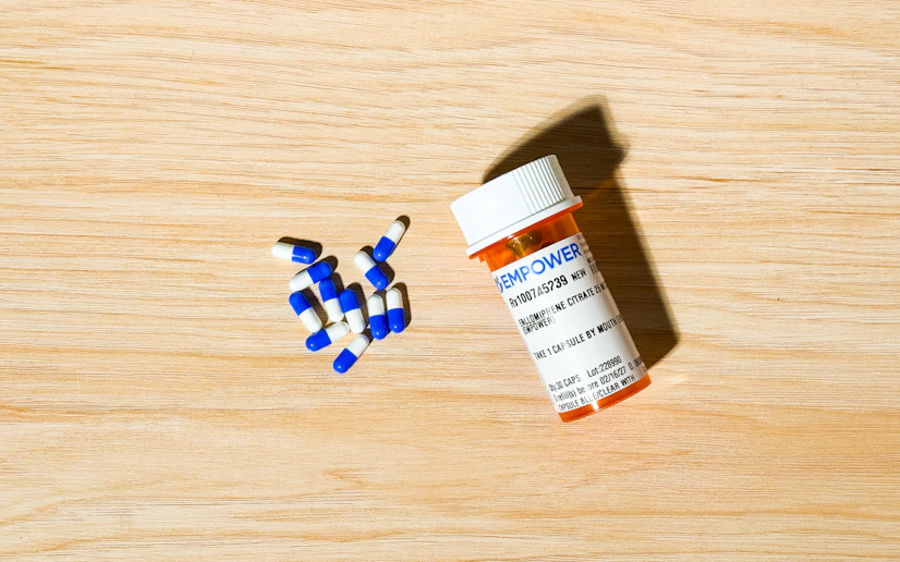 Medication bottle form 1st Optimal with its capsules poured out on a wood surface