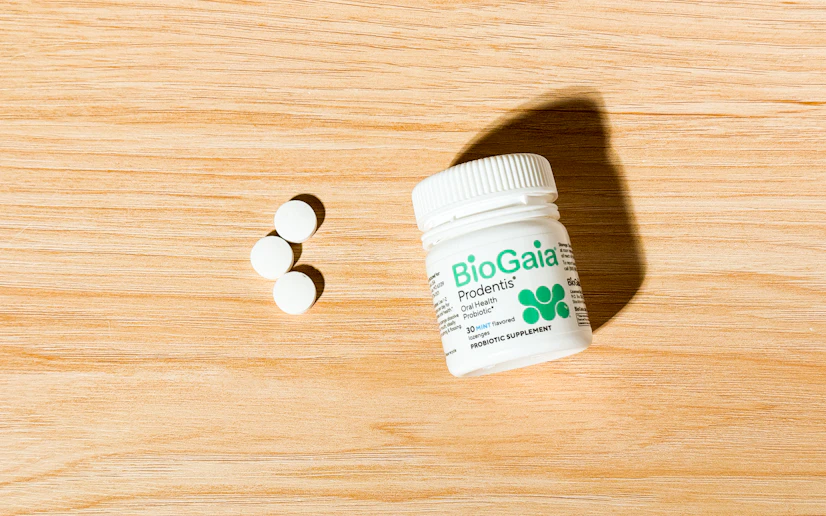 Biogaia Prodentis oral probiotic bottle and tablets on a wood surface.