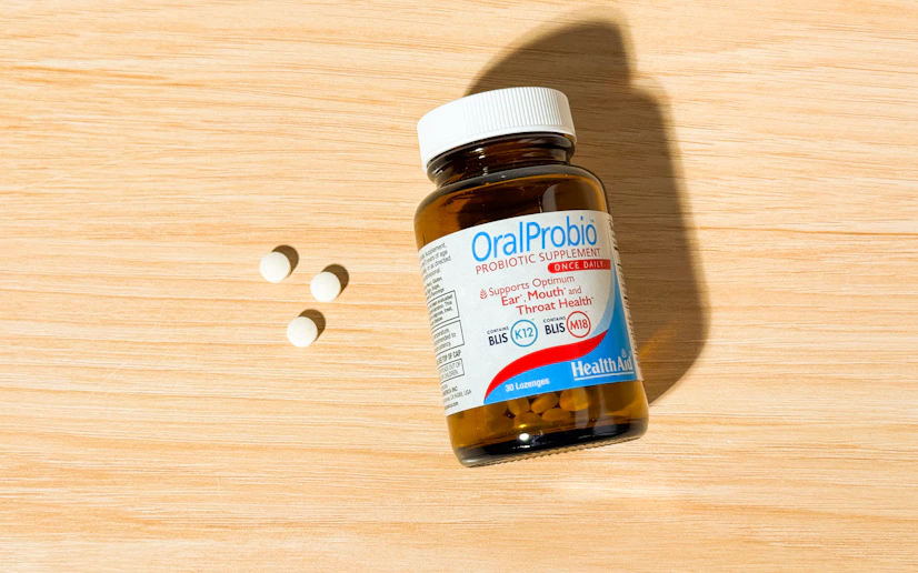 HealthAid OralProbio bottle and tablets on a wood surface.
