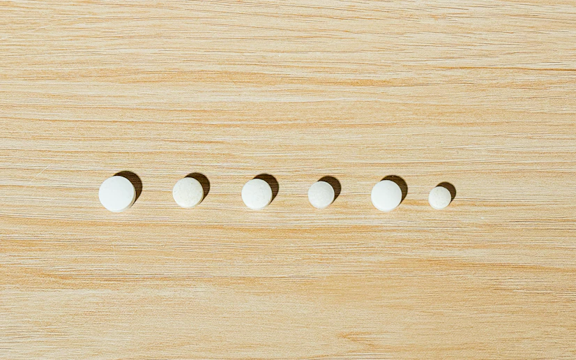 Several white tablets of the best oral probiotics lined up on a wood surface.