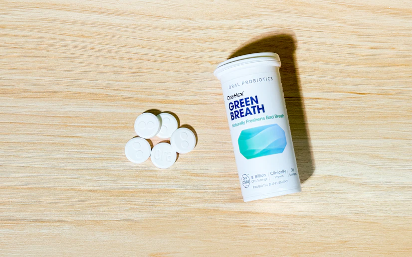 A tube of Oraticx Green Breath lozenges on a wooden surface with a few lozenges by its side.
