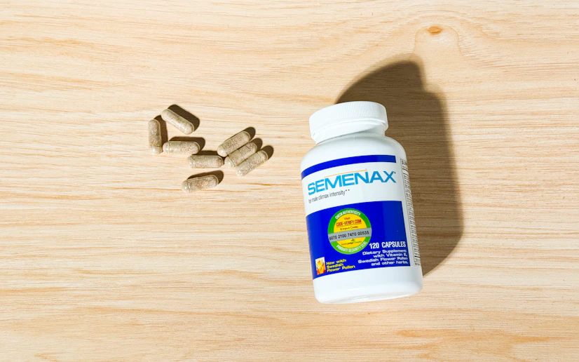 A bottle of Semenax with some of its capsules laid out on a wood surface