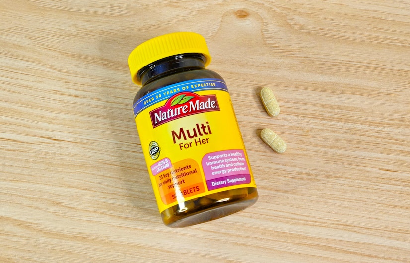 A top-down view of the Nature Made Multi For Her Tablets bottle on a wood countertop with two tablets