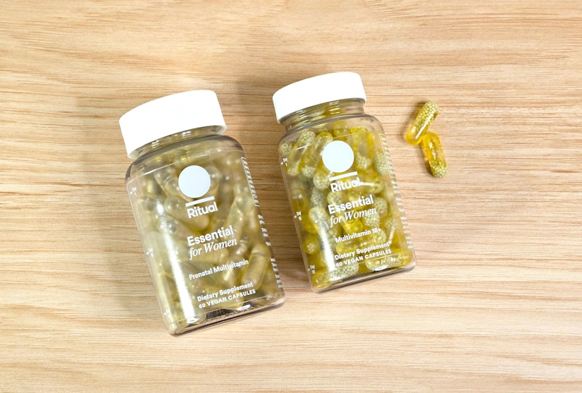 A top-down view of the Ritual Essential for Women 18+ and Ritual Essential Prenatal bottles on a wood countertop with two capsules
