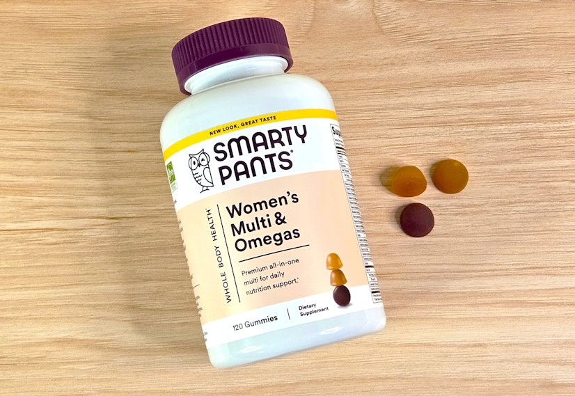 A top-down view of the SmartyPants Women's Multi & Omegas bottle on a wood countertop with three gummies