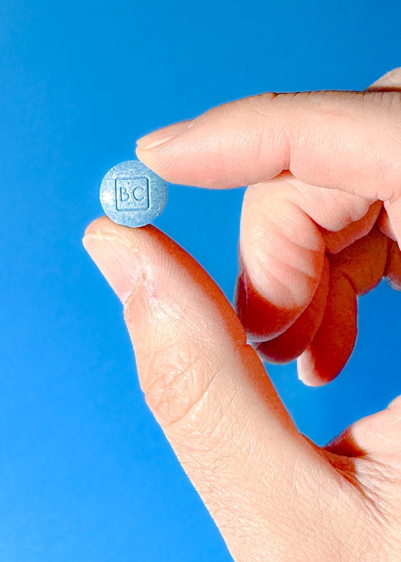 A BlueChew chewable tablet held between a man's thumb and forefinger against a blue background.