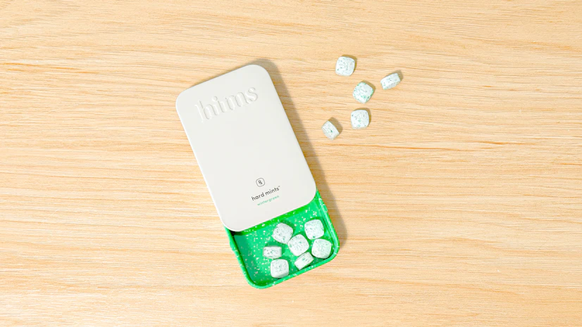 A top-down shot of Hims Hard Mints Tin with mints spilled out on wood surface