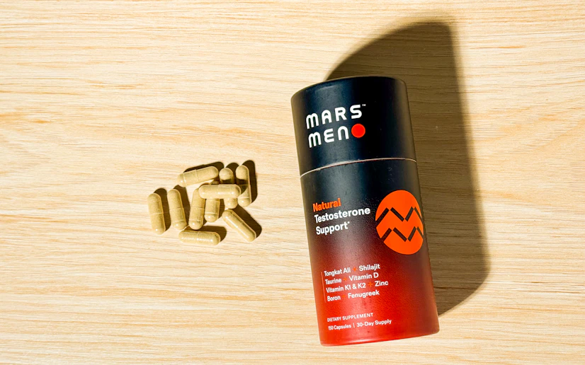 One bottle of Mars Men and some of its capsules laid out on a wood surface.