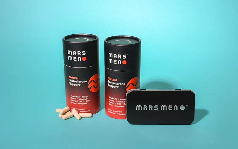 two bottles of Mars Men Testosterone Booster alongside a travel tin and some loose capsules against a blue background.
