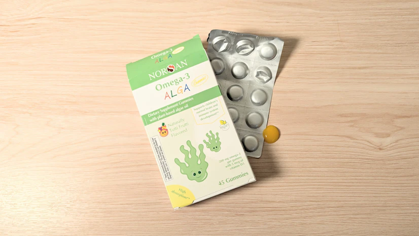 Box and blister pack of Norsan Omega-3 Alga Gummies on a wood surface.