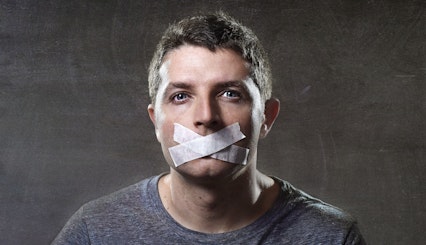 An adult man with paper tape in an “X” over his mouth, symbolizing how male victims of abuse are often silenced.