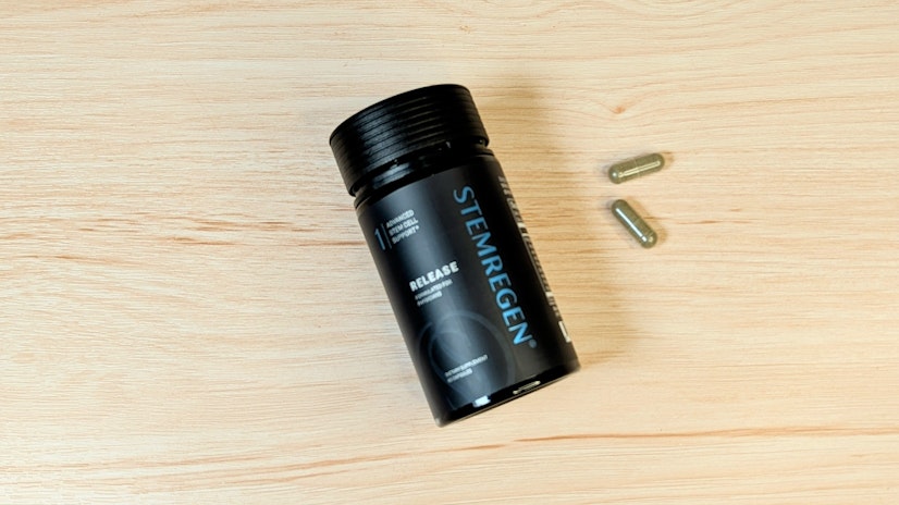 Bird’s-eye view of a bottle of STEMREGEN Release next to two capsules, on top of a wooden surface.