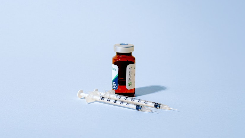 A small brown vial labeled Tailor Made Compounding and two syringes lie on a light blue background