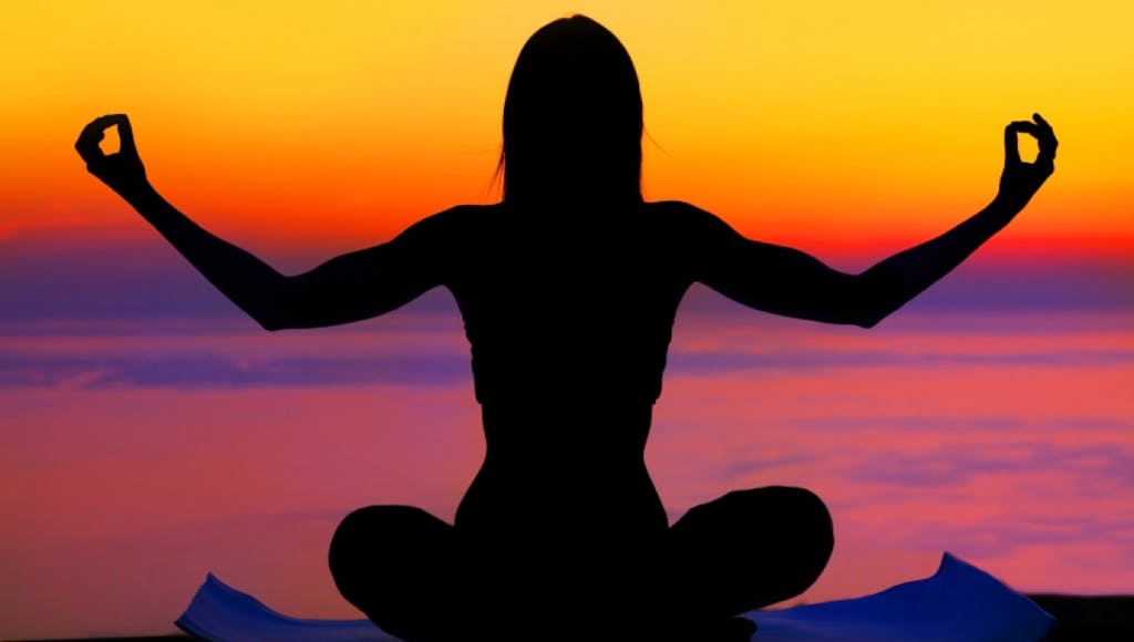 woman doing yoga on a mat in front of a sunset